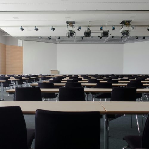 Spacious contemporary conference room with rows of tables and chairs, ready for meetings.