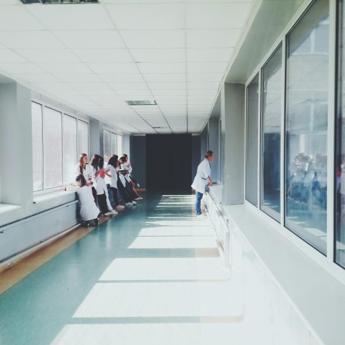 A brightly lit hospital hallway with medical staff in white coats, conveying a professional healthcare environment.