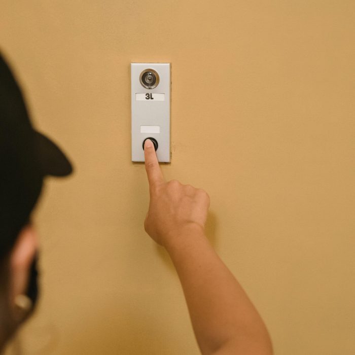 pexels-photo-9461215-9461215 Close-up of a person pressing a doorbell on a beige wall, emphasizing hand action.